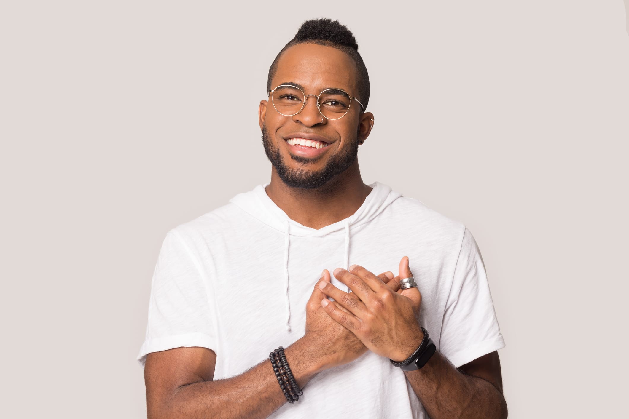 Happy smiling young african american guy in eyeglasses crossing hand on chest near heart, demonstrating thankful gesture, appreciation. Grateful handsome man posing on grey studio background.